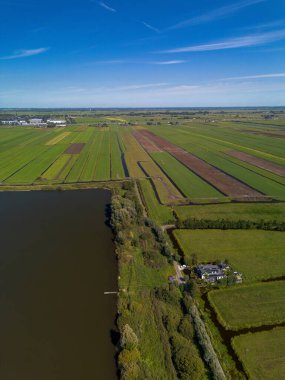 Merkezi yolu, su birikintisi, sulama alanları ve dağınık evleri olan kırsal bir arazinin havadan görünüşü. Sahne tarım planlaması ve doğal bütünleşmeyi vurguluyor.