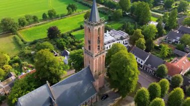 Kırmızı kiremitli çatıları, yemyeşil yeşillikleri ve merkezinde uzun bir kilise kulesi olan büyüleyici bir Avrupa kasabasının havadan görünüşü. Dar sokaklar ve rahat evler huzurlu, resimli bir manzara yaratır..