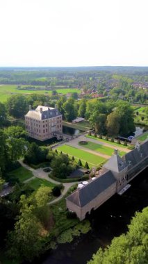 Çevrelenmiş hendek adasındaki tarihi bir şatonun havadan görünüşü, resmi bahçeler, emlak binaları ve yeşil tarlalar, su yolları ve resimli kırsal bir manzara arasında yer alan yakınlardaki bir kasaba..