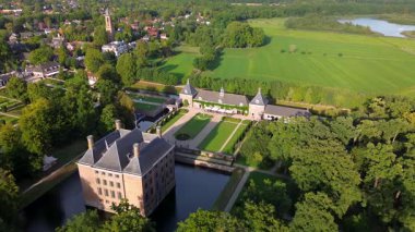 Çevrelenmiş hendek adasındaki tarihi bir şatonun havadan görünüşü, resmi bahçeler, emlak binaları ve yeşil tarlalar, su yolları ve resimli kırsal bir manzara arasında yer alan yakınlardaki bir kasaba..