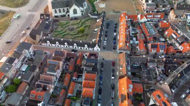 Beyaz bir kilisesi, kırmızı çatılı evleri ve manzaralı bir avlusu olan kıyı kasabasının havadan görünüşü. Kumsal, kum tepeleri ve sahil kulübeleri kıyı boyunca uzanır. Mimariyi doğayla harmanlarlar..