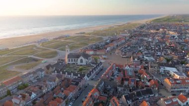 Beyaz bir kilisesi, kırmızı çatılı evleri ve manzaralı bir avlusu olan kıyı kasabasının havadan görünüşü. Kumsal, kum tepeleri ve sahil kulübeleri kıyı boyunca uzanır. Mimariyi doğayla harmanlarlar..