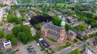 Ağaçlar, yollar ve karışık kullanım binalarıyla çevrili yeşil kulesi olan Gotik bir kilisenin havadan görünüşü. Taş mimarisi bu iyi korunmuş kentsel alanda göze çarpıyor..