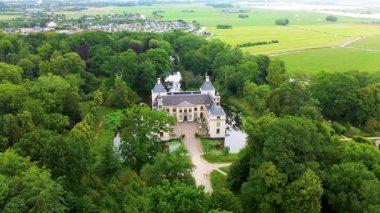 Bir hendek, resmi bahçeler ve daha küçük redroofed binalar ile çevrili, beyaz, şatoya benzeyen bir malikane, yoğun ağaçlar ve açık arazilerle çevrili,.