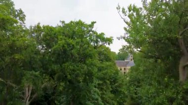 Bir hendek, resmi bahçeler ve daha küçük redroofed binalar ile çevrili, beyaz, şatoya benzeyen bir malikane, yoğun ağaçlar ve açık arazilerle çevrili,.