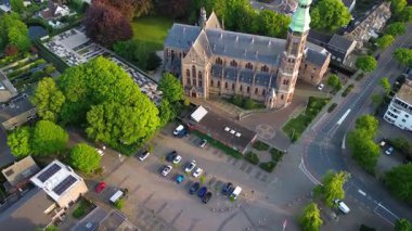 Ağaçlar, yollar ve karışık kullanım binalarıyla çevrili yeşil kulesi olan Gotik bir kilisenin havadan görünüşü. Taş mimarisi bu iyi korunmuş kentsel alanda göze çarpıyor..