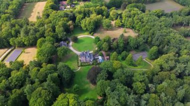 Merkezi malikane, dairesel garaj yolu, bitişik binalar, güneş panelleri ve geleneği, doğayı ve sürdürülebilirliği harmanlayan çevredeki alanların havadan görünüşü.