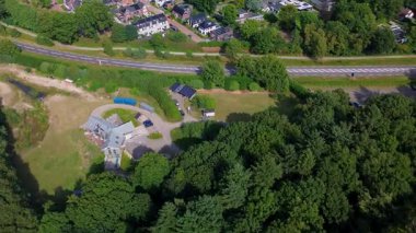 Eğri araba yolu, park etmiş araçlar, evler, yeşillik ve göl manzaralı arazi kullanımı ve organize banliyö planına sahip yarı kırsal mahalle manzarası.