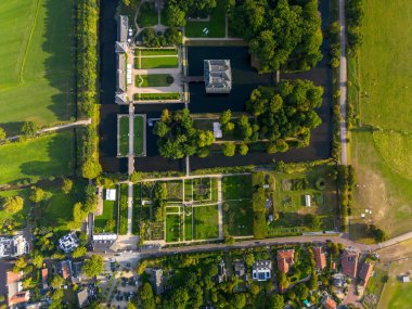 Simetrik bahçeleri, köprüleri ve dikdörtgen binaları olan, orman, tarla ve su ile çevrili, tarihi tasarım ve manzara uyumunu gösteren havadan manzaralı bir arazi..