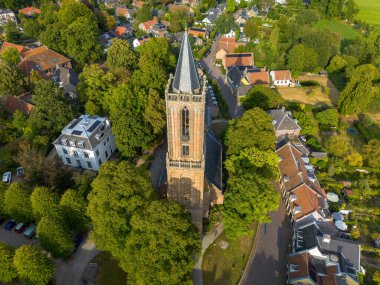 Şehrin merkezi Gotik tarzı kilisesi, çan kulesi, kırmızı ve gri çatıları, ağaçlarla kaplı caddeleri ve modern hayatla harmanlanmış park edilmiş arabaları olan hava manzarası..