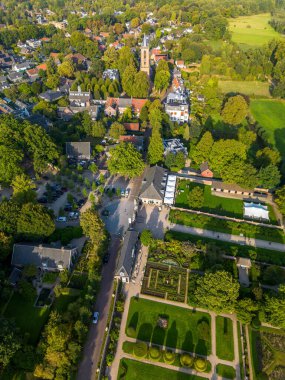 Yüksek çan kulesi kilisesi, resmi bahçesi, ağaç kaplı caddeleri ve mimari ile doğal tasarım arasındaki ahengi gösteren tarihi binaların havadan görünüşü..