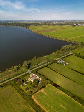 Kırsal arazinin havadan görünüşü, sulama alanları, göl evi, bahçe ve uzak kıyı şeridi ile uyumlu arazi kullanımı ve su yönetimi.