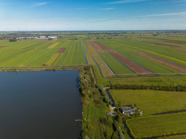 Merkezi yolu, su birikintisi, sulama alanları ve dağınık evleri olan kırsal bir arazinin havadan görünüşü. Sahne tarım planlaması ve doğal bütünleşmeyi vurguluyor.