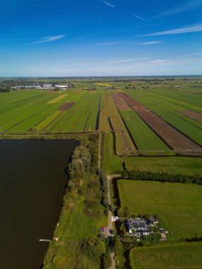 Merkezi yolu, su birikintisi, sulama alanları ve dağınık evleri olan kırsal bir arazinin havadan görünüşü. Sahne tarım planlaması ve doğal bütünleşmeyi vurguluyor.