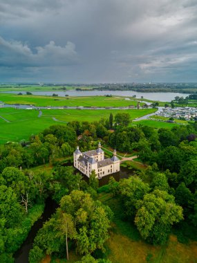 Hendeklerle çevrili tarihi şatonun havadan görünüşü, yoğun yeşillikler, modern evler ve mimari mirası çağdaş kırsal alanlarla harmanlayan kesişen su yolları..