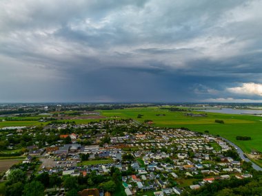Çiftlik arazisi ve su yoğunluğundaki konutlarla çevrili hava manzarası park edilmiş arabalar ve çarpıcı fırtına bulutları canlı yeşil alanlar ve kırsal açıklıkla tezat oluşturuyor..