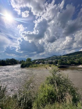 Dağ nehri ve yeşil ağaçlar yazın beyaz bulutlu mavi gökyüzünün arka planına karşı..