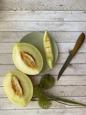 Yarım tatlı ballı kavun, bir dilim kavun, tahta masada bıçak.