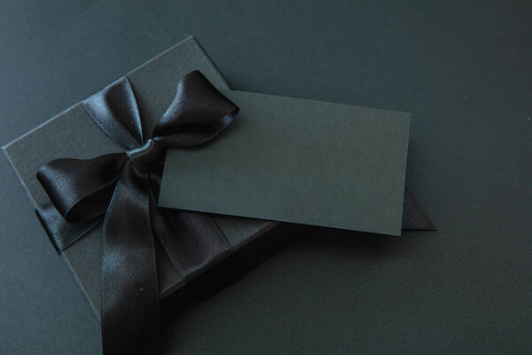 Black Friday Sale and Christmas presents. Gift box with black ribbon and empty card isolated against black background,