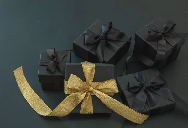 Black Friday sales promotion concept. Five gift box one with luxury golden ribbon and four with black satin ribbon on black background,