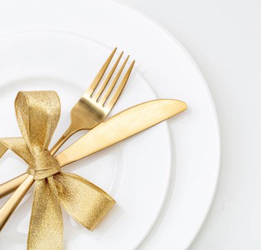 Noel masası manzarayı ayarlıyor. Altın çatal bıçak takımı ve beyaz tabaklar, şık bir restoran, kutlama yemeği.