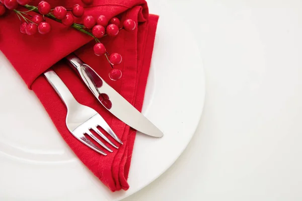 Holiday table setting. Silver Cutlery and red cloth napkin on white plate, close up view. Christmas New Year celebration dinner