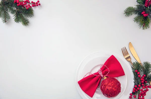 Christmas table setting, celebration dinner flat lay. Golden Cutlery, red cloth napkin and Xmas decoration on white background, top view, copy space