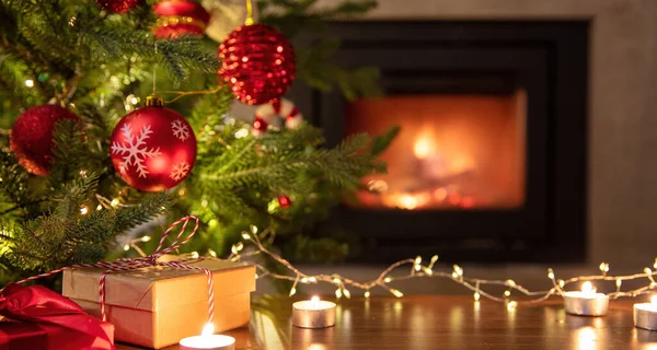クリスマスツリーの装飾とクリスマスはテーブルの上に提示し 暖炉の背景を燃焼し スペースをコピーします 冬のお祝い — ストック写真