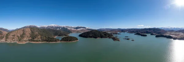 Greece, Lake Aoos Springs, Epirus. Aerial panoramic drone view of artificial lake near Metsovo village. Snowy Pindus mountain background.