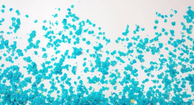 Confetti bright blue scattered on white background. Carnival party, festive decoration, invitation card. Space for text. Overhead view.
