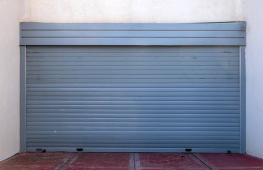 White wall with blue empty roller shutter door background. Metal garage door construction, closed foldable entrance, red entry floor, safety. Space