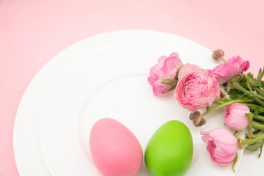 Mutlu Paskalya kutlaması masaları. Paskalya yumurtaları ve düğün çiçekleri tabakta çiçek süslemesi, pastel pembe arka plan,