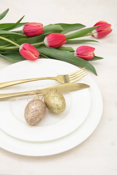 复活节餐桌摆设 红郁金香和复活节彩蛋装饰 盘子上的金色餐具 白色背景 — 图库照片