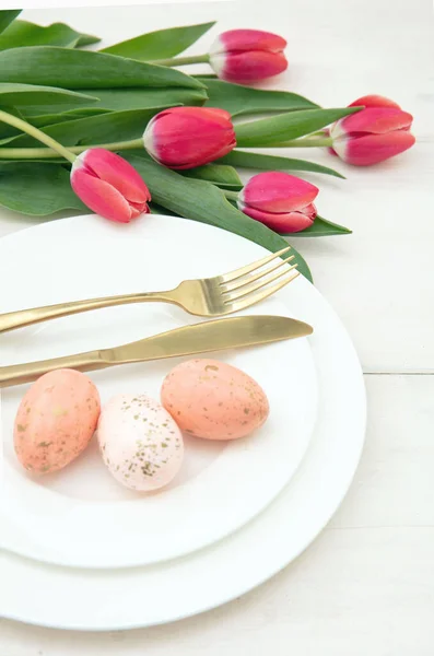 Easter table setting, Spring flowers and eggs decoration, golden cutlery on plates, white background