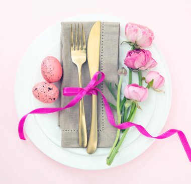 Paskalya sofrası, Paskalya yumurtası ve çiçek süslemesi, beyaz tabaklarda peçete ve altın çatal bıçak takımı, pastel pembe arka plan.