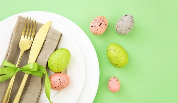 复活节餐桌摆设 复活节彩蛋装饰 餐巾和白盘上的金色餐具 淡绿色背景 — 图库照片