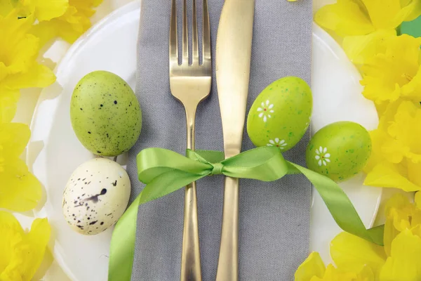 复活节餐桌布置 黄色春花和彩蛋装饰 餐巾和白色盘子上的金色餐具 闭合顶部视图 — 图库照片