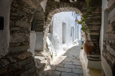 Tinos Adası Yunanistan. Kikladik mimari Kardiani köyünde, kemerli taş duvar dar kaldırım taşlı sokak, beyaz duvarları kaplıyor. Dikey