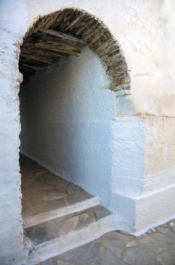 Tinos Adası, Dio Choria Köyü, Yunanistan. Eski ahşap kemerli duvar dar asfalt koridoru kapatıyor. Kiklad beyazlatılmış taş duvar. Dikey