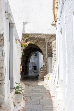 Tinos Adası Yunanistan. Kikladik mimari Kardiani köyünde, kemerli taş duvar dar kaldırım taşlı sokak, beyaz duvarları kaplıyor. Dikey