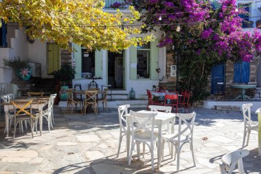 Dio Horia köyü Cyclades Yunanistan 'daki Tinos Adası' ndaki açık hava geleneksel kafe. Asfalttaki ahşap masa sandalyesi, bina arka planı, bougainvillea.