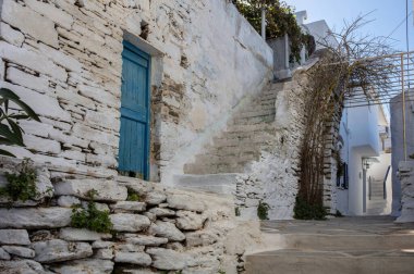 Yunanistan. Tinos Adası, Dio Horia köyü. Beyaz ve mavi renkli sikladik mimari, taş duvarlı ev ile açık gökyüzü arkaplanı arasındaki dar merdiven..