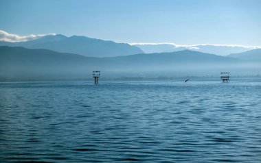 Yunanistan Pamvotis Gölü, Ioannina şehri Epirus. Durgun suda mavinin tüm tonları ve açık gökyüzü arkaplanı. Demir yapı kuşu barındırır.