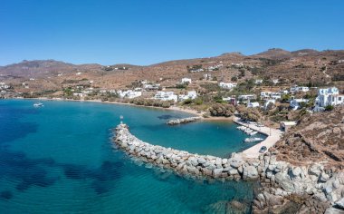 Tinos Adası, Cyclades Yunanistan. Agios Romanos köyünün insansız hava aracı görüntüsü, şeffaf mavi deniz, kayalık dalgakıran, körfez, limanda demirli tekne..