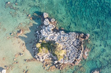 Sakin turkuaz deniz suyu arka planında kayalık oluşumu gösteren hava aracı görüntüsü. Okyanusun ortasında yeşil deniz yatağı olan Yunan gri kayası.