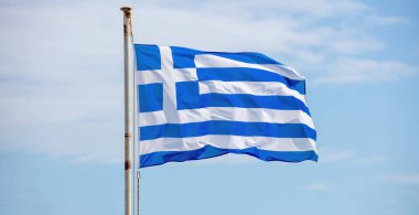 Yunanistan 'ın işareti. Rüzgarda dalgalanan paslı bayrak direğinde mavi-beyaz Yunan resmi bayrağı. Cyclades adasındaki bulutlu gökyüzü arkaplanı.
