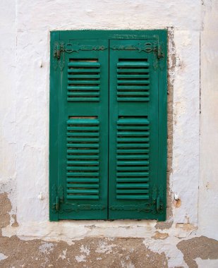 Solmuş, soyulmuş beyaz duvar zemininde kapalı yeşil ahşap panjurlu eski moda pencere. Ev cephesi, Cyclades Adası, Yunanistan. Dikey