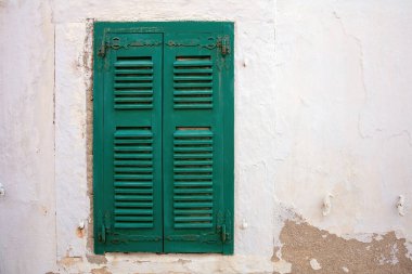 Solmuş, soyulmuş beyaz duvar zemininde kapalı yeşil ahşap panjurlu eski moda pencere. Ev cephesi, Cyclades Adası, Yunanistan. Boşluk