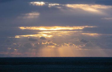 Deniz Burnu. Gün batımı arkaplanındaki bulutların arasından geçen altın güneş ışığı. Koyu mavi Ege Denizi. Kiklad adası Yunanistan.