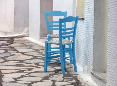 Yunanistan 'ın Cyclades adasında yaz günü beyazlatılmış taş duvar evinin önündeki asfalt dar sokakta iki boş ahşap sandalye..